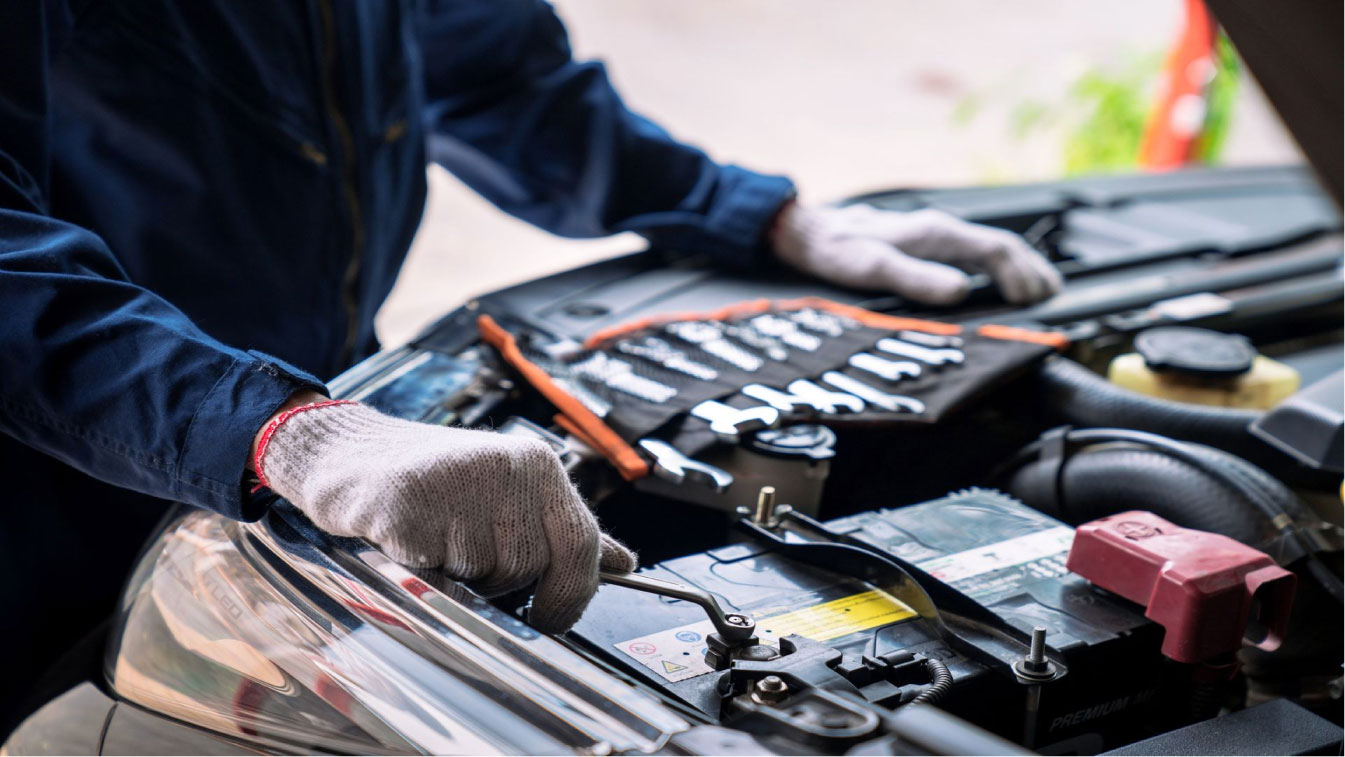 Mechanic fixing car battery with workers gloves and overalls. Finding battery under the hood of car.